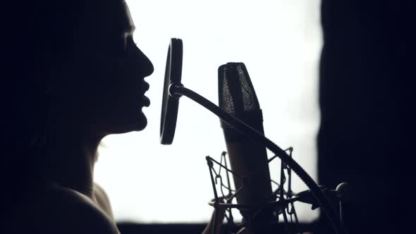 Silhouette of beautiful woman is singing a song in front of a microphone
