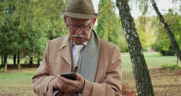 Elegant Senior Man Typing on Smartphone at Camera in Beautiful Sunny Park