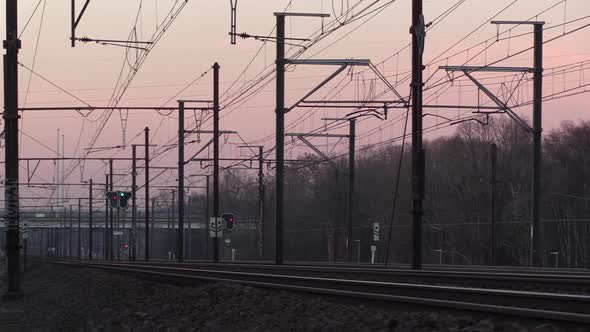 train tracks and catenary at sunset with passing cars over a distant bridge, creating a feeling of l