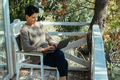 Middle-aged woman working on laptop computer sitting at table on wooden balcony of country house. - PhotoDune Item for Sale