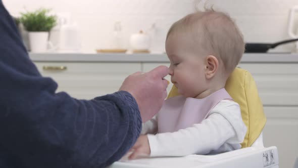 Father Feeding His Baby in the Kitchen at Home Closeup of Oneyearold Baby Boy in White High Baby