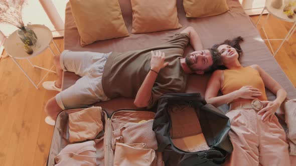 Couple and Suitcases Lying on Bed