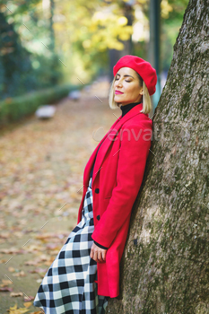 g elegant red outerwear leaning on tree trunk in autumn park
