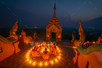 Group of young and senior monk sit in a circle with several lighting candle surround