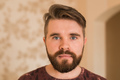 Portrait of an attractive young bearded hipster man looking at the camera standing in modern house - PhotoDune Item for Sale