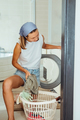 Young woman housekeeper sits in front of a washing machine. Household routine. - PhotoDune Item for Sale