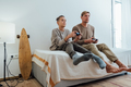 Father and teen son sitting on bed playing video game. Spending time together - PhotoDune Item for Sale