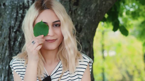 Blond Caucasian Girl Holding a Small Green Leaf Close to the Eye