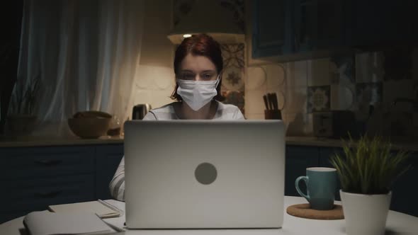 Young Girl In The Kitchen With Laptop, Woman In Medical Mask Makes Notes In Notepad