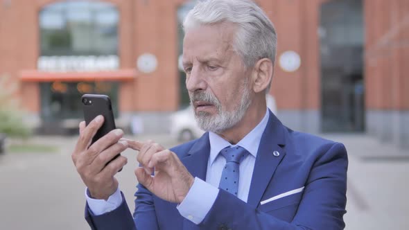 Outdoor Portrait of Old Businessman Upset By Loss on Smartphone