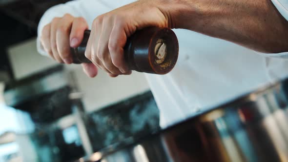 Close up: the chef is using pepper mill to add some pepper to food, pepper is falling in slow motion