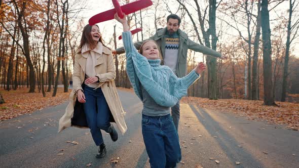 Young Mom and Dad Running with Little Daughter Holding Red Toy Plane