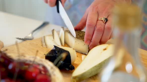 A Female Hand with a Knife Cuts Cheese on a Wooden Cutting Board