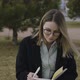 Portrait of smiling young girl in glasses sitting outdoors in a park and making notes in notebook - VideoHive Item for Sale