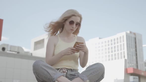 Woman Walking and Using a Smart Phone in the Street in a Sunny Summer Day