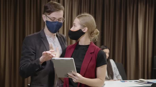 Young Man and Woman in Coronavirus Face Masks Talking Discussing Business Idea and Looking at Camera