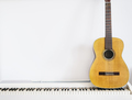 Acoustic guitar on piano keyboard in front of white wall.  - PhotoDune Item for Sale