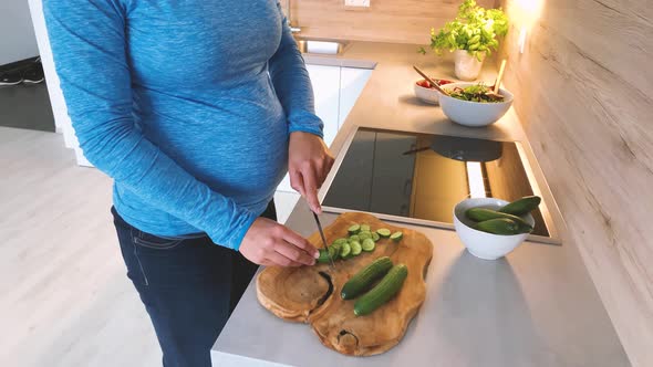 Slow motion shot of pregnant woman cutting cucumber in kitchen