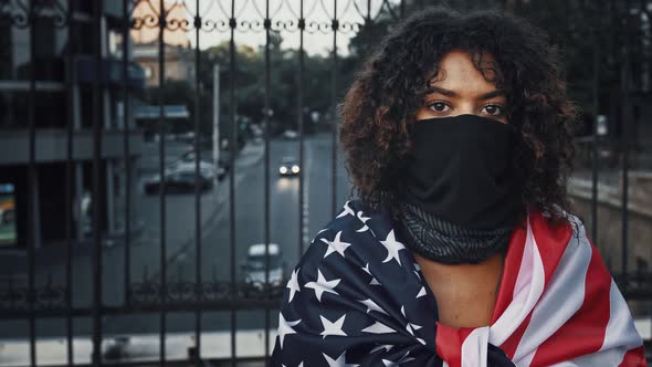 Darkskinned Female in Black Bandana on Face Wrapped in Flag of USA