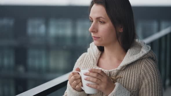 Woman Stays on Balcony During Snowfall with Cup of Hot Coffee or Tea