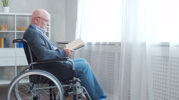 Disabled old man is sitting in a wheelchair at home alone. A handicapped person.