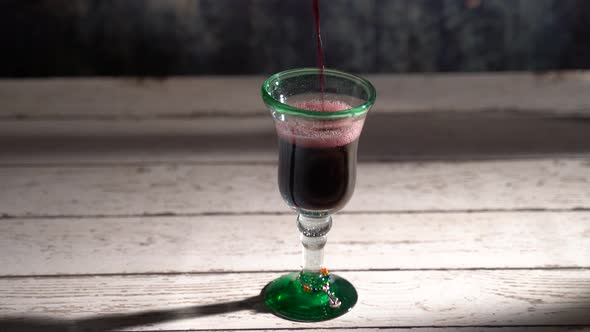 Seamless, looping clip of red wine pouring into a rustic glass with blue background.