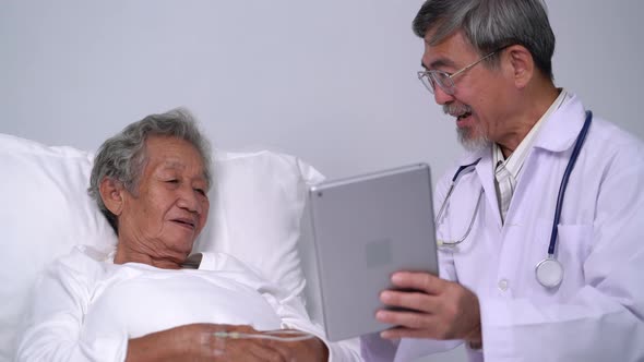 Asian man doctor using digital tablet explain the symptoms to the patient in hospital bed