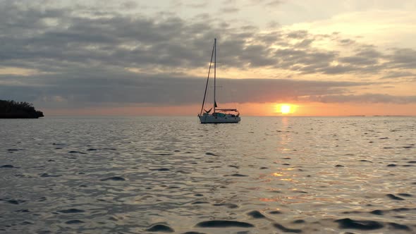 Cinematic Aerial View, Sailboat Anchored in Sea by Island Coast With Picturesque Sunset on Horizon,