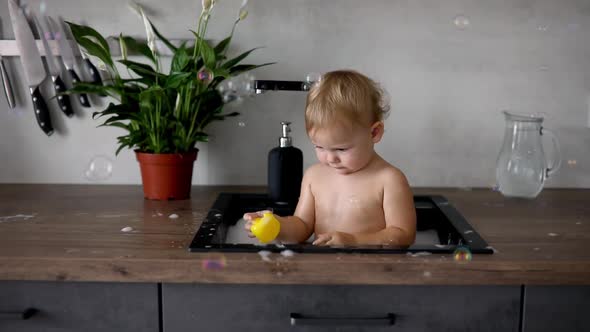 Cute Happy Baby Girl with Playing with Water and Foam in a Kitchen Sink at Home