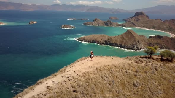 Two Young Women are Jumping Joyfully on the Top of the Mountain Hugging and Enjoyng the Ocean Beauty