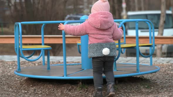 Lonely Little Kid Girl Gets in a Merrygoround at Children's Playground
