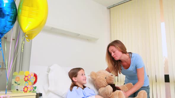 Smiling woman giving a teddy bear to a smiling girl in a bed