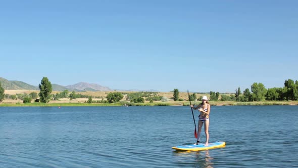 Young woman learning how to paddleboard on small pond.