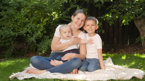 Older Boy Hugging His Baby Brother and Mother Sitting on Grass in Garden