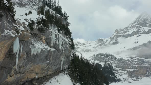 Aerial dolly from ice covered mountain wall to beautiful snow covered valley