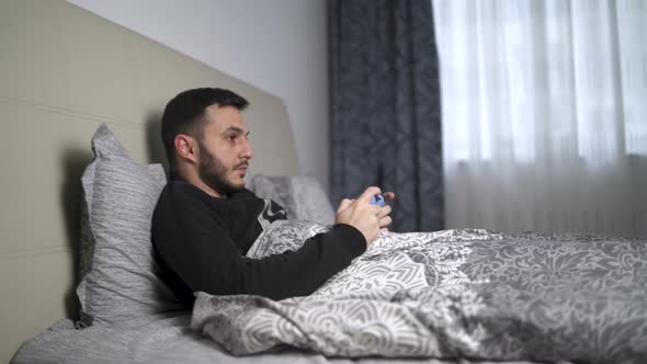 Quarantined Young Man Playing Video Games in Bed Using Controller