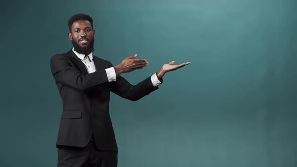 A Black Bearded Man in a Tuxedo is Posing Standing with a Thumbs Up and Looking at the Camera