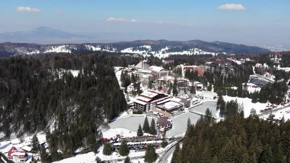 Flying over a frozen pond and famous hotels in Poiana Brasov ski resort on a sunny winter day