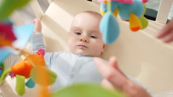 Little Baby By Lying in Crib with Colorful Toys and Holding Mother's Hand