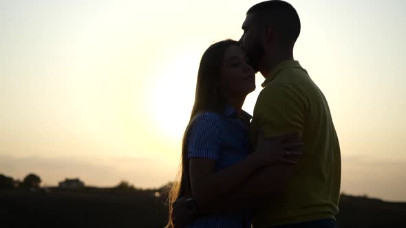 Silhouettes of a Bearded Young Man and His Girlfriend Hugging, Snuggling Together and Kissing. Young