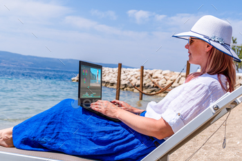 Editing Videos On Laptop Using Video Editor App. Young woman working abroad on laptop while sitting on the beach, video editing freelance working