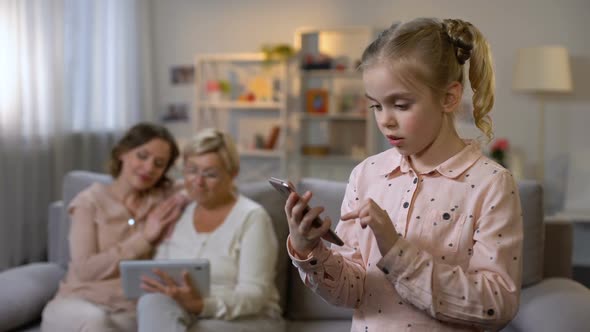 Smiling Child Using Smartphone App, Grandmother and Mother Scrolling Tablet