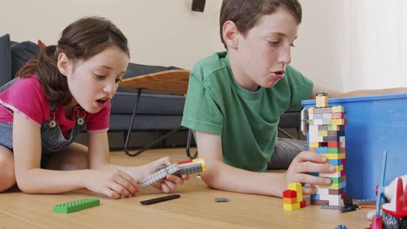 Girl and a boy playing and constructing with toy bricks on the living room floor