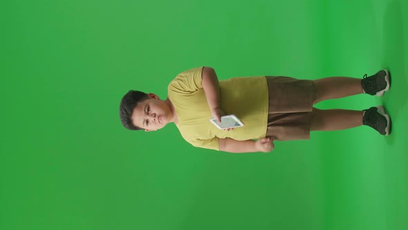 Full Body Of Bored Asian Little Boy Using Mobile Phone In Green Screen Studio