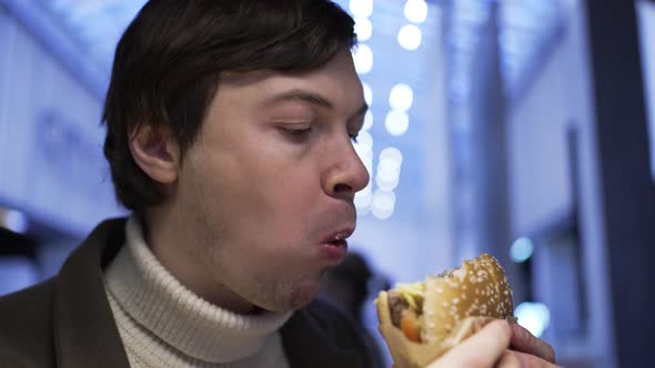 Side View of a Man Greedily Biting a Burger and Chewing in a Fast Food Restaurant