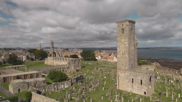 Aerial drone flying by one of the towers of the St Andrews Cathedral as other towers and the coastli