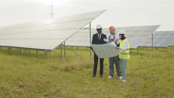 People in Hardhats Standing Outdoors Among Solar Cells and Having Working