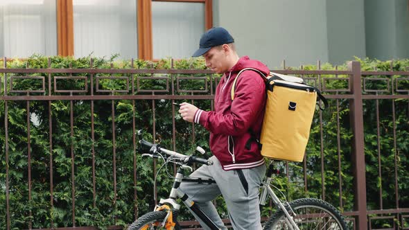 A Delivery Man with a Thermal Backpack Uses a Mobile Phone