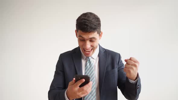 Happy Male Office Worker in Formal Clothes Uses Mobile Phone Rejoices in Victory