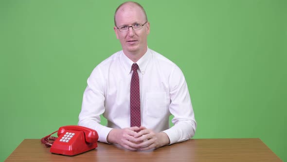 Mature Bald Businessman Interrupted By Phone Call Against Wooden Table